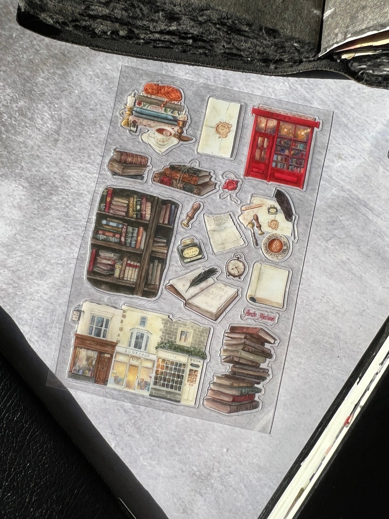 May include: A sheet of clear stickers featuring illustrations of books, a bookstore, a red mailbox, and other bookish elements. The stickers are perfect for adding a touch of whimsy to journals, planners, and other paper crafts.