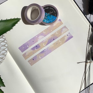 May include: Three rolls of washi tape with a purple and cream color scheme. The tape features a repeating pattern of clouds, stars, and crescent moons. The tape is labeled "Washi Tape" and has a small logo.