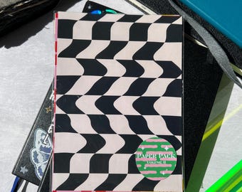May include: A stack of paper with a black and white checkered pattern. The paper has a sticker on it that says "Paper Pack Volume II" in green and pink letters.