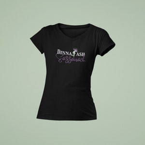 May include: Black v-neck t-shirt with the text "Dinna Fash Sassenach" in white lettering and a purple thistle graphic.