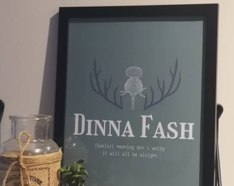 May include: A framed print with a blue background and white text that reads "Dinna Fash (Gaelic) meaning don't worry it will all be alright". The print features a stylised thistle with antlers on either side.