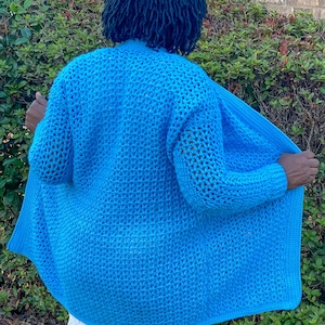 May include: A bright blue crocheted cardigan with a loose fit and open front. The cardigan is made with a lacy stitch pattern and has long sleeves.