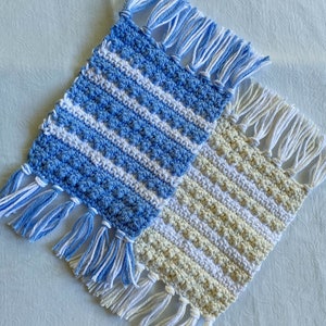May include: Two crocheted coasters with fringe. One is blue and white, the other is beige and white.