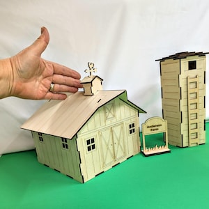 Puede incluir: Un modelo de madera de un granero con un silo y un letrero que dice "Anderson Farm". El granero tiene una veleta en la parte superior y una puerta con una ventana. El silo tiene una escalera en el lateral. El modelo está hecho de madera marrón claro.