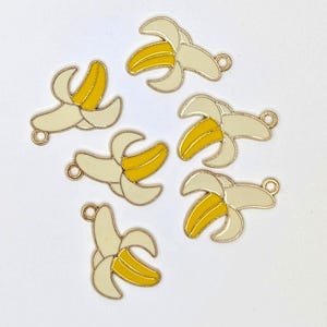 May include: Six gold-coloured banana charms with a yellow peel and cream-coloured peel. Each charm has a small loop at the top for attaching to jewellery or other crafts. The bananas are in various stages of being peeled.