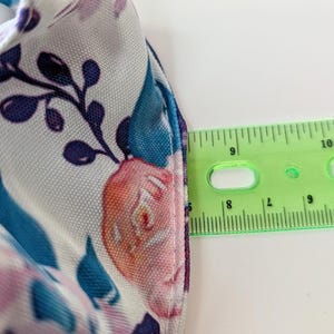 May include: Close-up of a floral patterned fabric with a ruler showing measurements. The fabric features a white background with teal, purple, and pink floral designs. The ruler shows a measurement of approximately 2.5 cm.