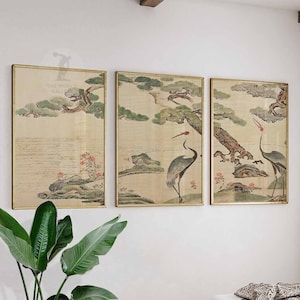 以下が含まれることがあります： 鶴、木、水を描いた伝統的な日本の風景を描いた、額装された3つのアートプリント。アートワークは、金色のフレームで、落ち着いた色合いが特徴です。プリントは白い壁に展示されており、穏やかな美しさを生み出しています。