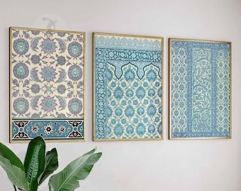 May include: Three framed wall art pieces with intricate floral and geometric patterns in shades of blue, teal, and cream. The artwork is displayed on a white wall, with gold frames, and a touch of greenery in the foreground.