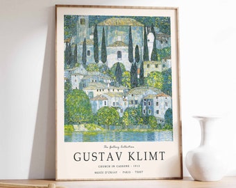 May include: A framed poster of a painting by Gustav Klimt titled "Church in Cassone" from 1913. The painting depicts a village with a church in the background, surrounded by trees and a lake. The poster is on a wooden table with a white vase.