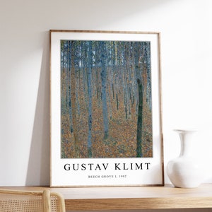 May include: A framed print of a painting by Gustav Klimt titled "Beech Grove I, 1902". The painting depicts a forest scene with tall, slender trees in shades of blue and green. The ground is covered in a layer of fallen leaves in shades of yellow and brown.