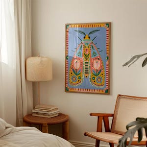 Pode incluir: Uma impress&atilde;o art&iacute;stica emoldurada com uma ilustra&ccedil;&atilde;o colorida e estilizada de uma mariposa. A obra de arte tem um fundo azul com um desenho central de mariposa em tons de laranja, rosa, amarelo e verde. A moldura &eacute; em tom de madeira natural.