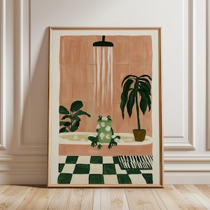 May include: A framed wall art print depicting a green frog sitting in a bathtub filled with white bubbles under a shower head. The bathroom features peach-coloured tiled walls and a floor with a green and white checkered pattern, with two potted plants.