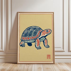 Op de afbeelding: Ingelijste kunstdruk met een gestileerde schildpadillustratie. De schildpad heeft een blauw en rood schild, rode kop en poten, tegen een beige achtergrond met een rode rand. Het kunstwerk zit in een houten lijst.