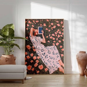 K&ouml;nnte beinhalten: Ein gro&szlig;er gerahmter Kunstdruck zeigt eine Person, die in einem Blumenfeld liegt und ein Tablet h&auml;lt. Die Person tr&auml;gt ein rosa Kleid mit floralem Muster. Das Kunstwerk wird in einem Raum mit einer Pflanze, einem Ottoman und dekorativen Vasen ausgestellt.