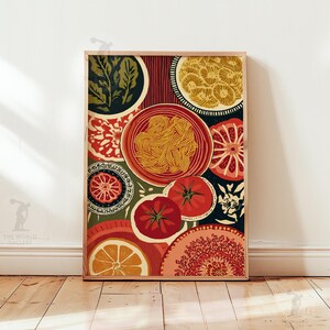 May include: A framed art print featuring a colorful, stylized illustration of food items. The artwork includes plates of pasta, tomatoes, citrus slices, and decorative patterns in shades of red, orange, green, and yellow. The print is displayed on a wooden floor.