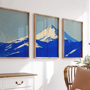 K&ouml;nnte beinhalten: Drei gerahmte Kunstdrucke mit einer Berglandschaft in Blau-, Wei&szlig;- und Beiget&ouml;nen. Das Kunstwerk hat eine Vintage-&Auml;sthetik, wobei die Gipfel und H&auml;nge des Berges im Mittelpunkt stehen. Die Rahmen sind aus hellem Holz gefertigt.
