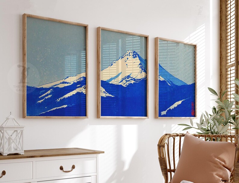K&ouml;nnte beinhalten: Drei gerahmte Kunstdrucke mit einer Berglandschaft in Blau-, Wei&szlig;- und Beiget&ouml;nen. Das Kunstwerk hat eine Vintage-&Auml;sthetik, wobei die Gipfel und H&auml;nge des Berges im Mittelpunkt stehen. Die Rahmen sind aus hellem Holz gefertigt.