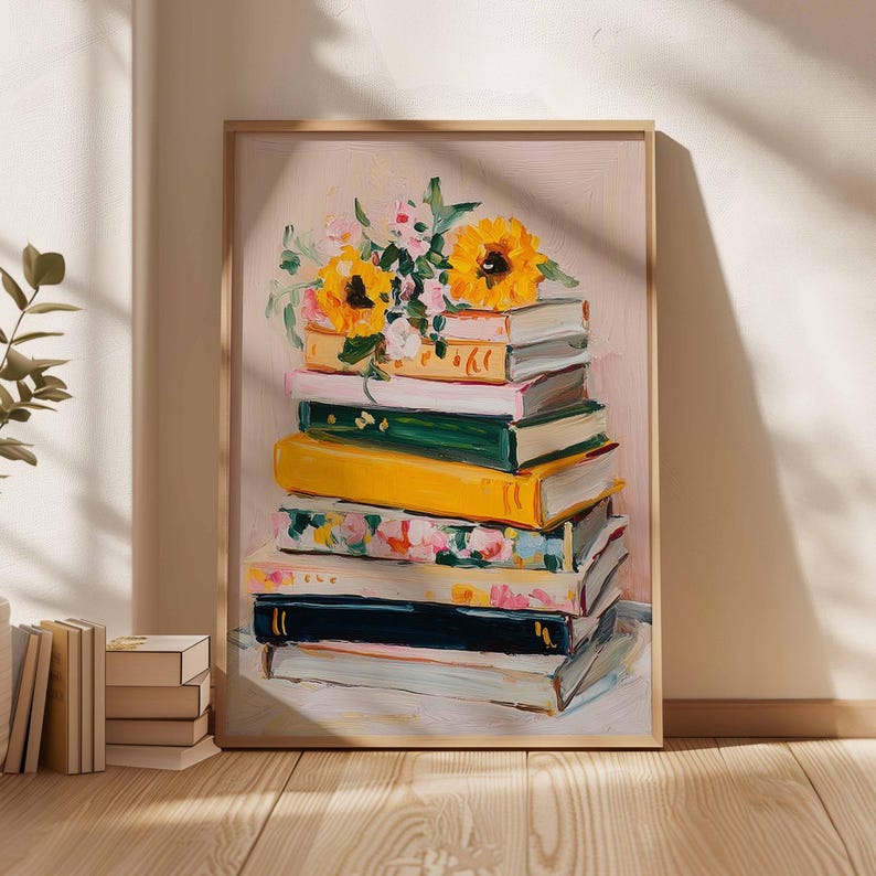 May include: A framed art print featuring a stack of books with a bouquet of sunflowers and other flowers on top. The books are painted in various colors, including yellow, green, and floral patterns. The background is a soft pink.