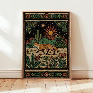 May include: A framed art print featuring a desert landscape with a fox. The artwork has a black background with a sun, cactus, and various plants. The fox is orange and brown, and the frame is a light brown color.