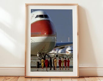 May include: A framed print featuring a vintage airplane with a red and white nose. A group of people in colorful dresses and suits stand in front of the plane. The image is set against a clear sky.