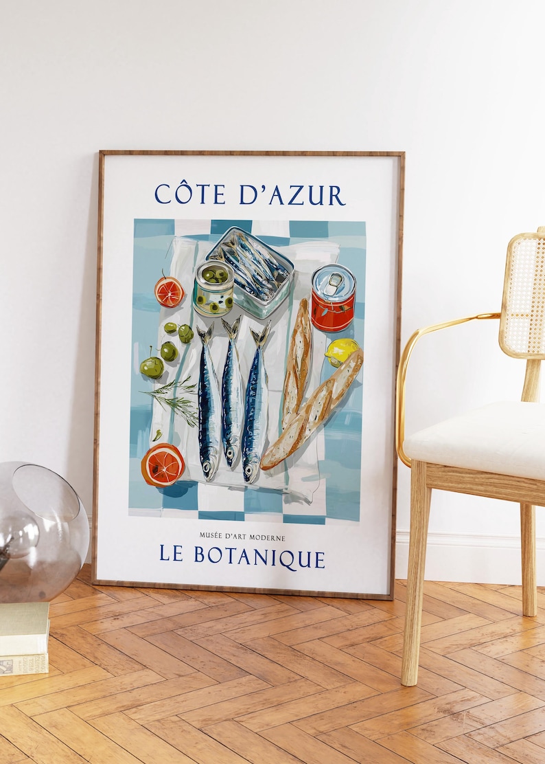 May include: A framed art print featuring a still life of food items. The image includes sardines, olives, bread, and citrus fruits on a blue and white checkered cloth. The text "C&Ocirc;TE D'AZUR" and "LE BOTANIQUE" are visible.