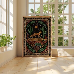 May include: A framed art print featuring a desert landscape with a fox, cacti, and sun. The artwork has a black background with orange, green, and yellow accents. The print is displayed in a bright room with a window.