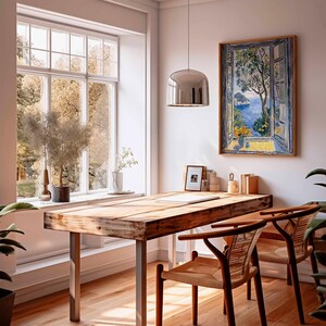 Puede incluir: Una mesa de madera con un acabado r&uacute;stico, dos sillas con asientos tejidos y una pintura enmarcada de un paisaje mar&iacute;timo con vista a una ventana. La mesa tiene una l&aacute;mpara colgante plateada colgando sobre ella.