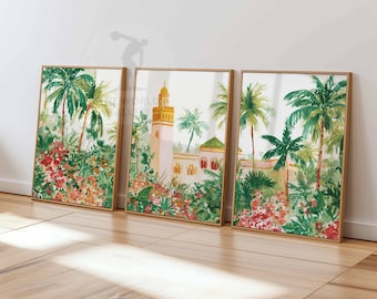 May include: Three framed watercolor prints featuring a Moroccan architectural scene with a minaret, palm trees, and lush red and green foliage. The artwork is set against a white background, with a wooden frame.