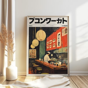 May include: Framed print of a Japanese restaurant interior. The artwork features a chef behind a wooden counter, with hanging lanterns and red curtains. The print has Japanese text at the top.
