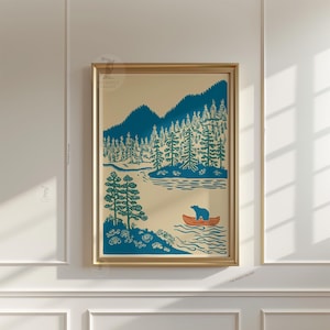 May include: A framed art print featuring a blue and orange illustration of a bear in a canoe on a lake, surrounded by trees and mountains. The artwork has a vintage, outdoorsy theme, with a cream-colored background and a gold frame.