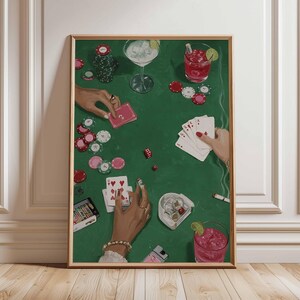 May include: A framed art print depicting a poker game scene. The green felt table is scattered with playing cards, poker chips, dice, and cocktails. Hands are visible, holding cards and chips. The artwork has a vintage, illustrative style.