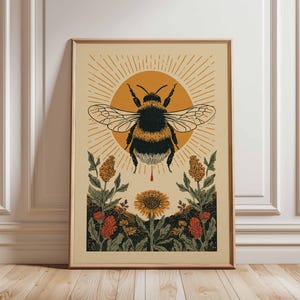 May include: Framed art print depicting a bumblebee illustration with a sunburst backdrop. The bee is black and yellow, with a red drop beneath. The artwork includes orange and green flowers and foliage, creating a nature-inspired theme.