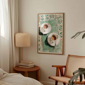May include: A framed art print depicts two white coffee cups with saucers, filled with coffee, on a green and white tiled surface. The artwork is in a wooden frame, suggesting a cafe or kitchen theme.
