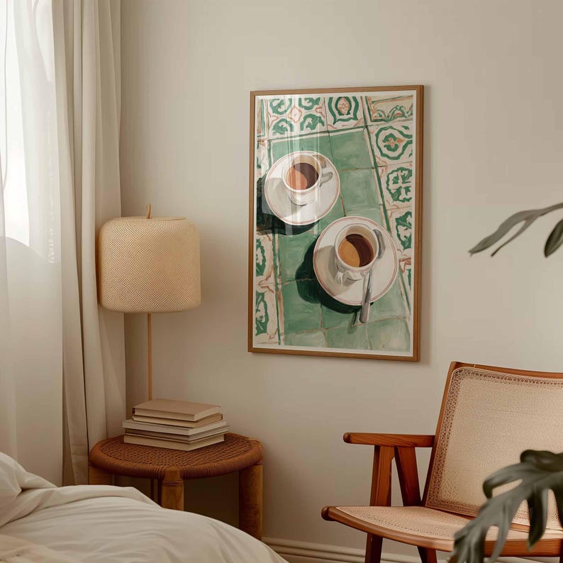 May include: A framed art print depicts two white coffee cups with saucers, filled with coffee, on a green and white tiled surface. The artwork is in a wooden frame, suggesting a cafe or kitchen theme.