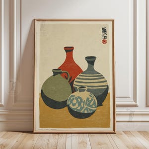 May include: Framed art print featuring a still life of four ceramic vases in shades of red, green, blue, and cream. The vases are arranged on a yellow surface against a cream background. Japanese text and a red seal are in the upper right corner.