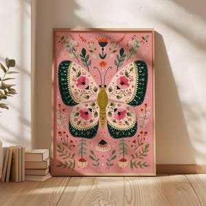 May include: A framed art print featuring a detailed illustration of a butterfly with floral patterns. The butterfly has pink, green, and cream-colored wings, set against a pink background. The artwork is surrounded by botanical elements.