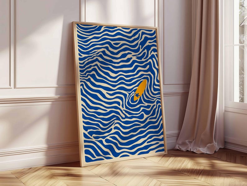 May include: Abstract art print featuring a blue and cream wavy pattern with an orange surfboard. The artwork is framed in a light wood frame and leans against a white wall and wooden floor. The art print adds a modern touch to any space.