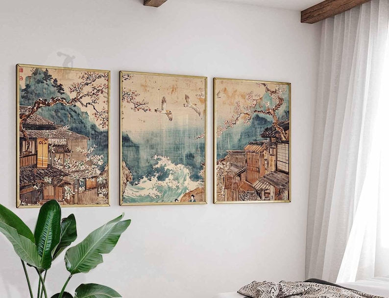May include: A set of three framed prints depicting a Japanese landscape with traditional houses, cherry blossoms, and a view of the ocean. The prints are in a muted color palette with shades of blue, green, and brown.