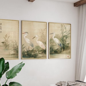 Può includere: Tre stampe artistiche incorniciate con dipinti ad acquerello di aironi bianchi in un ambiente paludoso. L'opera d'arte ha un'estetica vintage con cornici dorate e una tavolozza di colori neutri. Le stampe sono esposte su una parete bianca.