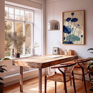 May include: A bright, airy interior with a wooden desk and two chairs. A framed floral print in blue and white hangs on the wall. A large window offers a view of trees. A silver pendant light hangs above the desk.