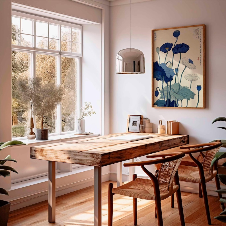 May include: A bright, airy interior with a wooden desk and two chairs. A framed floral print in blue and white hangs on the wall. A large window offers a view of trees. A silver pendant light hangs above the desk.