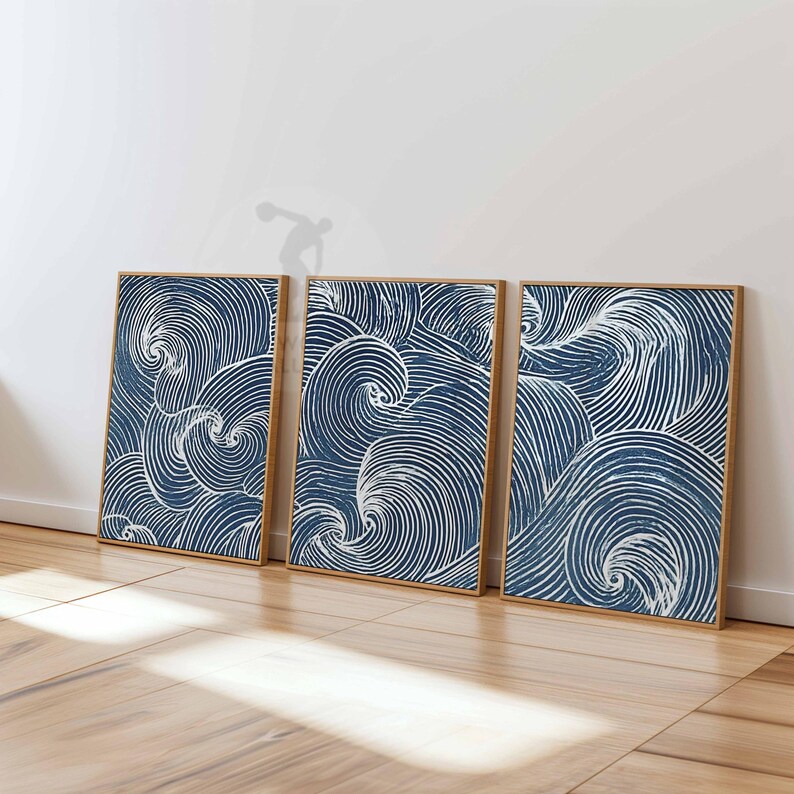 May include: Three framed art prints with a blue and white wave pattern. The artwork features swirling lines in a navy blue background, creating a dynamic and textured effect. The frames are a natural wood color, adding warmth to the overall aesthetic.