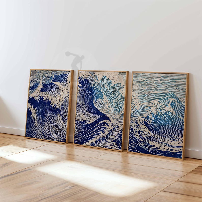 May include: Three framed prints featuring a stylized depiction of ocean waves in shades of blue and beige. The artwork has a woodblock print aesthetic, with detailed lines and textures. The frames are a light brown color.