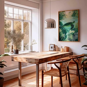 May include: A bright, airy room with a wooden desk and two chairs. A framed sea turtle art piece hangs on the wall. A large window offers a view of trees. A silver pendant light hangs above the desk. Plants and decor add to the room's aesthetic.