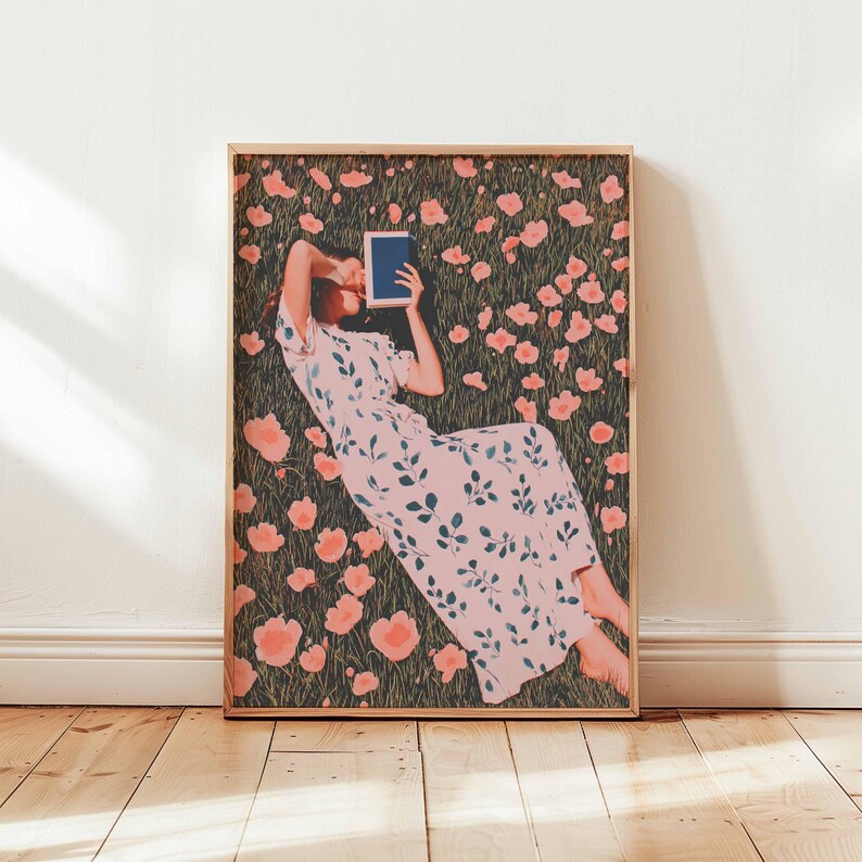 K&ouml;nnte beinhalten: Ein gerahmter Kunstdruck zeigt eine Person, die in einem Feld mit rosa Blumen liest. Die Person tr&auml;gt ein hellrosa Kleid mit einem blauen Bl&auml;ttermuster. Das Kunstwerk ist in einem hellbraunen Holzrahmen gerahmt.