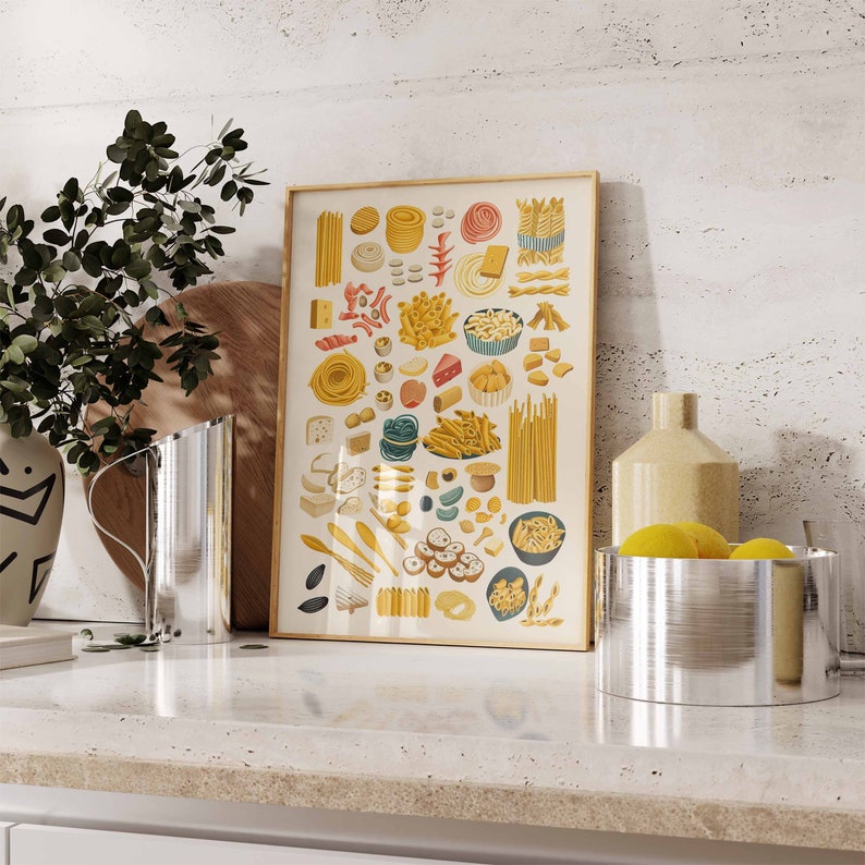 May include: A colourful illustration of different types of pasta, including spaghetti, penne, and rigatoni. The illustration is framed in a light wood frame and is displayed on a white countertop.