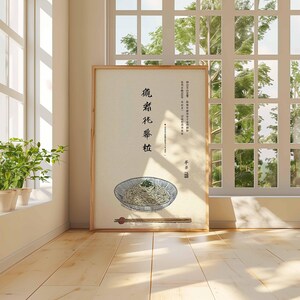 May include: A framed print featuring a bowl of noodles with chopsticks, set against a light background. The print includes Chinese characters and is displayed in a room with a window and plants.