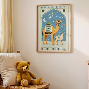 May include: A framed art print featuring a camel and a baby camel under a starry night sky. The artwork has a light blue background with a decorative arch and a wooden frame. The print is hanging on a white wall.