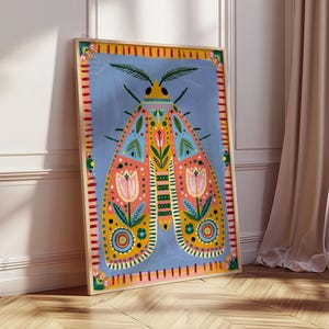 Pode incluir: Uma impress&atilde;o art&iacute;stica emoldurada com uma ilustra&ccedil;&atilde;o colorida de uma mariposa. A mariposa tem um corpo azul com detalhes em laranja, amarelo e rosa. A obra de arte est&aacute; em um fundo azul claro e emoldurada em uma moldura de madeira.