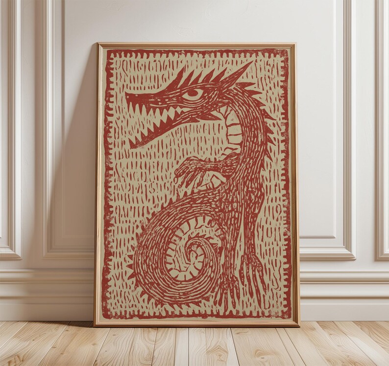 May include: A framed print featuring a red dragon illustration. The dragon has sharp teeth, a long neck, and a curled tail. The artwork is set against a textured beige background and framed in a wooden frame. The print is displayed on a wooden floor.